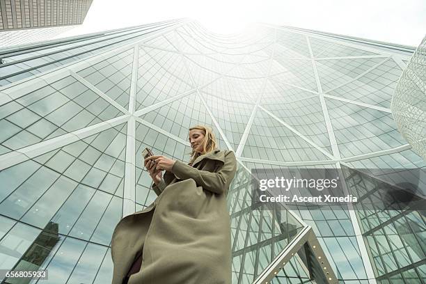 woman sends text on smart phone, city center - immeuble moderne photos et images de collection