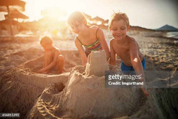 tres niños construyendo castillos de arena en la playa - castillo de arena fotografías e imágenes de stock