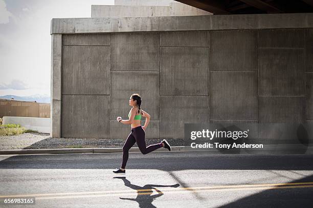 young woman running under freeway overpass - run up stock pictures, royalty-free photos & images