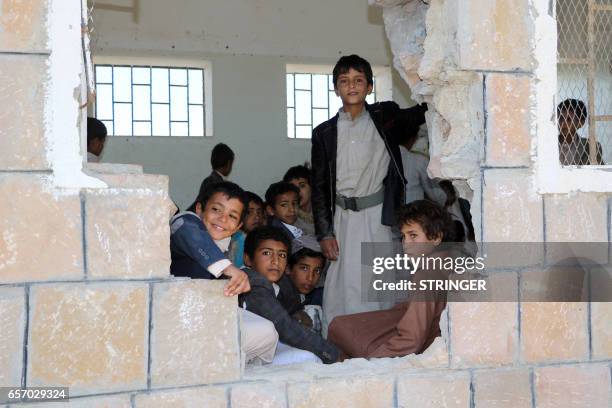 Yemeni students look out of a hole in the wall of a classroom that was damaged in the country's ongoing conflict between the Saudi-led Arab coalition...