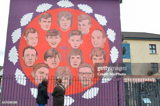 Two ladies await on the street in front of one of many murals for the coffin of former Northern Ireland Deputy First Minister Martin McGuinness, in...