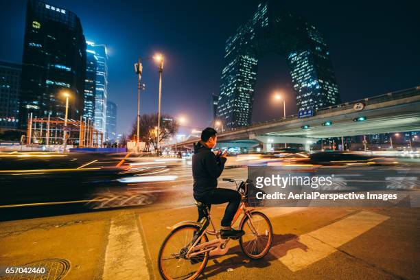 man looking at mobile phone on a bike at night - beijing city photos et images de collection