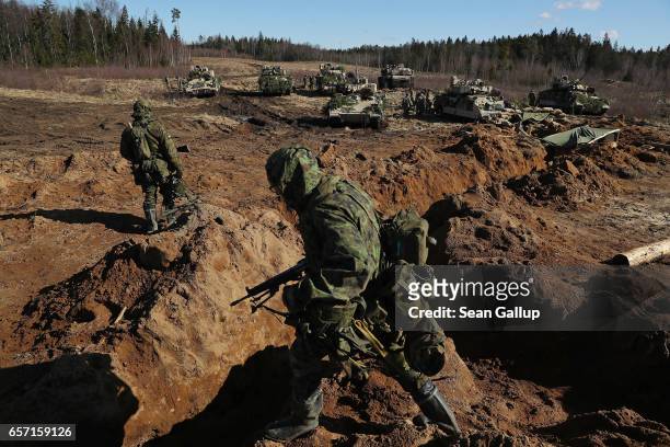 Estonian soldiers walk over a trench as US Army M2A3 Bradley fighting vehicles and an M1 Abrams tank stand behind following a joint military combat...