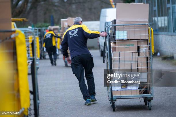 Postal workers pull carts loaded with parcels towards distribution vehicles at a Deutsche Post AG delivery station in Hamburg, Germany, on Tuesday,...