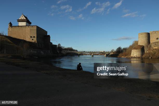 Man sits on the western bank of the Narva River below Hermann Castle and opposite Ivangorod Fortress, which is on the Russian side the Narva River,...