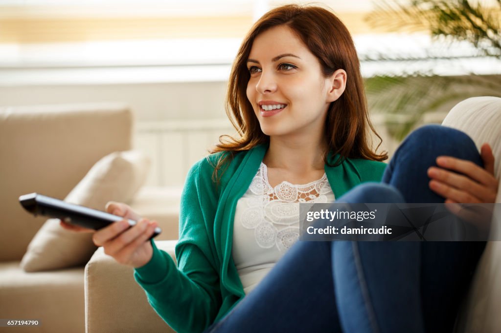 Jovem mulher assistindo TV em casa a sorrir