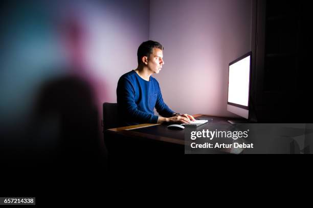 guy working at night in dark room in big screen computer sitting in office and focus on the screen with the only light of the computer and his shadow on the wall. - person on computer in dark room foto e immagini stock