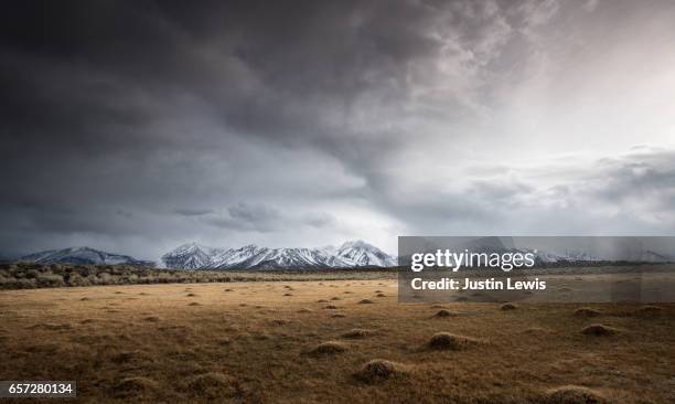 open field shows evidence of geothermal activity, snow-capped mountains in distance, stormy sky - day lewis imagens e fotografias de stock