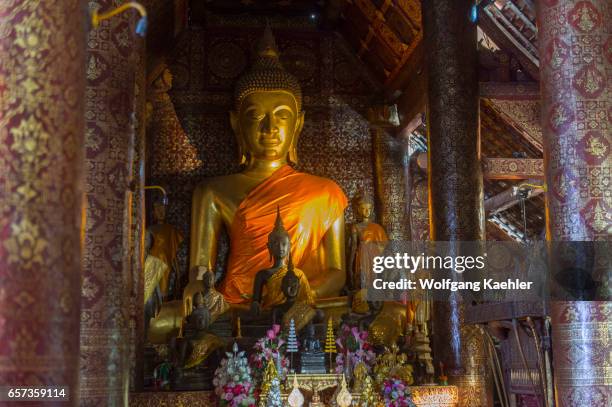 Seated on an elaborate pedestal is the principal Buddha statue in the Bhumisparsha mudra, surrounded by many smaller statues in the sim building of...