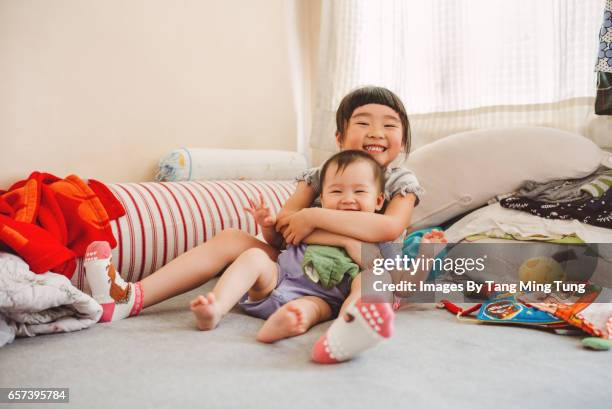 Lovely little girl hugging and playing with her baby sister on the bed while smiling at the camera joyfully