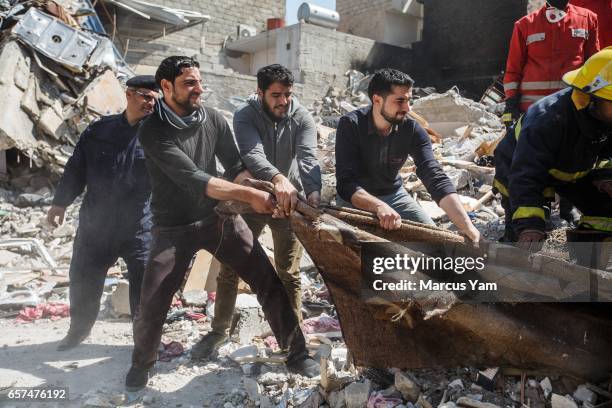 Family members help out the Iraqi civil defense force members pull out the corpses trapped underneath the rubble after there were reported coalition...