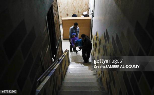 Two Syrian men carry 14-year-old Syrian Dania, who suffers from renal insufficiency, to have her dialysis treatment session inside a...