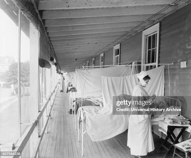 Masked Nurse at the Head of a Row of Beds Treating Patient during Influenza Pandemic, Walter Reed Hospital, Washington DC, USA, Harris & Ewing, 1918.