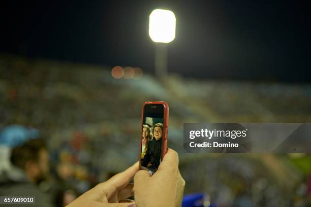 young couple at soccer match taking selfie portrait - teléfono inteligente stock-fotos und bilder