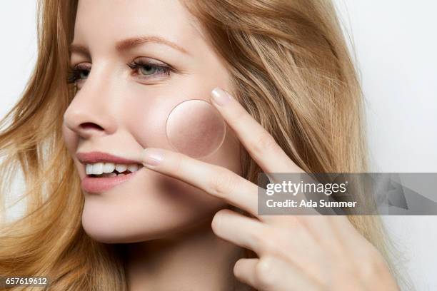 beautiful woman with flawless skin holding a magnifying glass over a part of skin with acne - brufolo foto e immagini stock