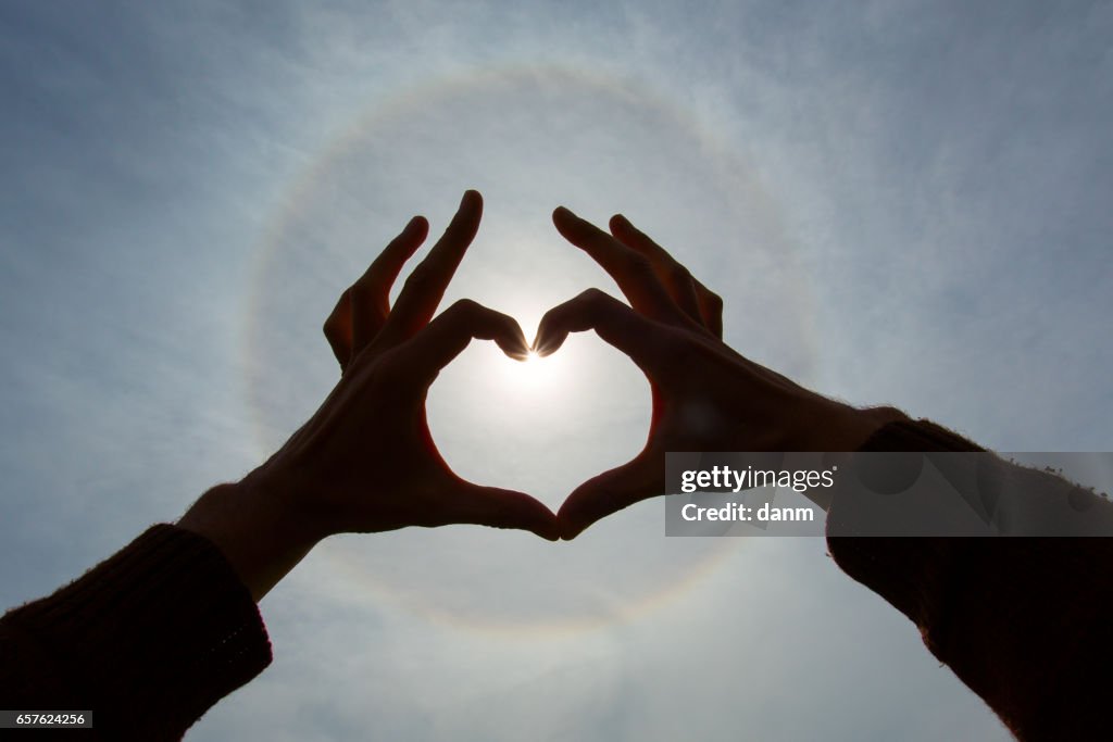 Lovers holding hands in shape of heart over a sunbow
