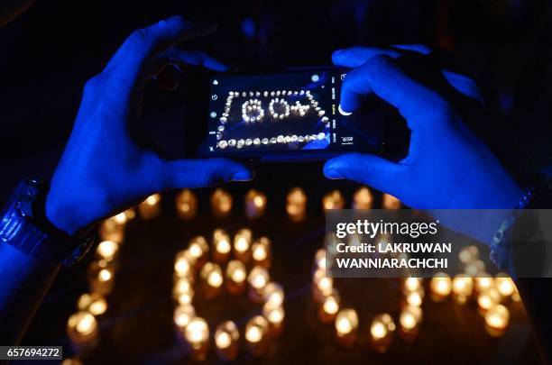 Sri Lankan man takes a picture after lighting up oil lamps to mark Earth Hour in Colombo on March 25, 2017. Millions of people were expected to...