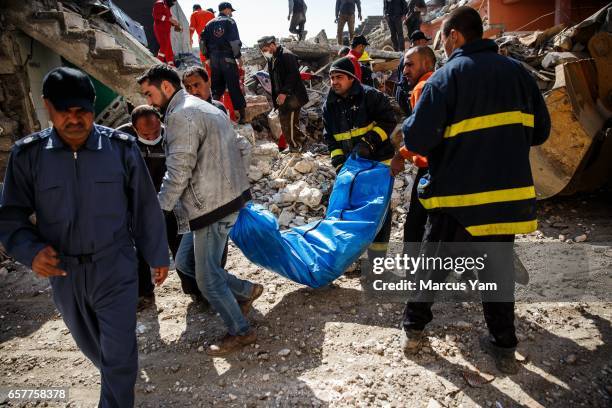 With the help of family members, Iraqi civil defense force members recover a dead body buried in the rubble of a home destroyed by reported coalition...