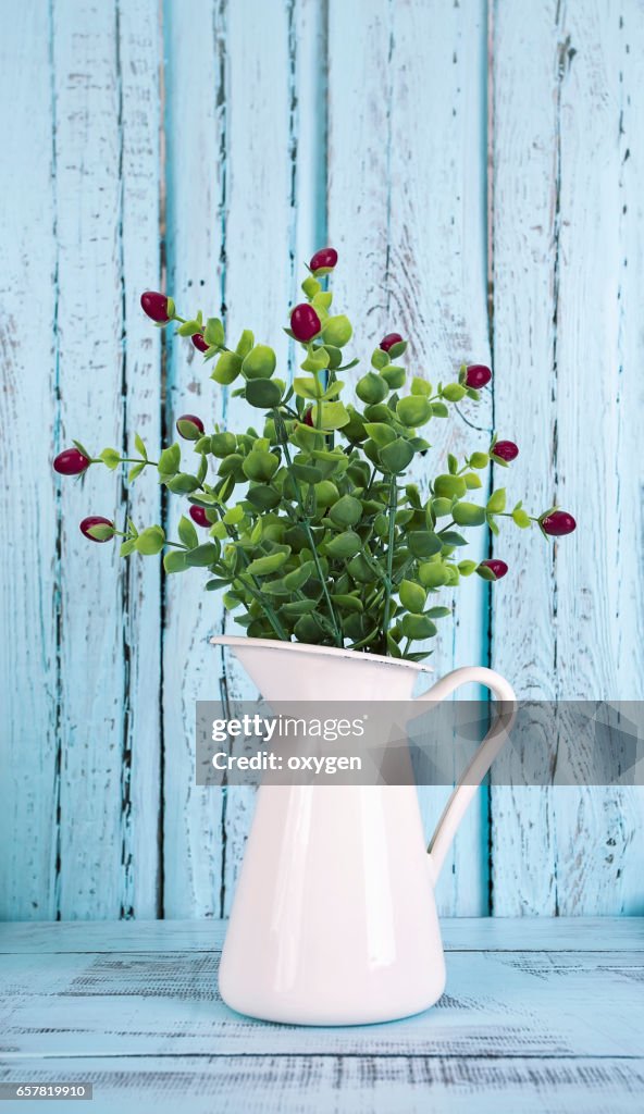 Jug with flowers on blue wooden background