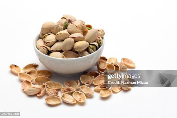 ceramic bowl filled with pistachios on white background. - nutshell stock pictures, royalty-free photos & images