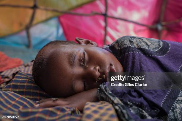 March 7, 2017: A young child covered in flies sleeps in a hot tent in a internally displaced persons camp in central Mogadishu. Somalia is in the...