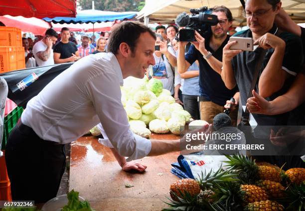 French presidential election candidate for the En Marche! movement Emmanuel Macron examines a piece of fruit during a visit to Le Chaudron market on...
