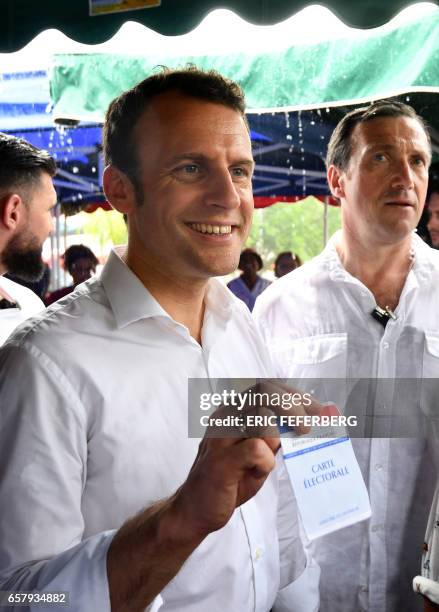 French presidential election candidate for the En Marche! movement Emmanuel Macron holds up a voting card during a visit to the Le Chaudron market on...