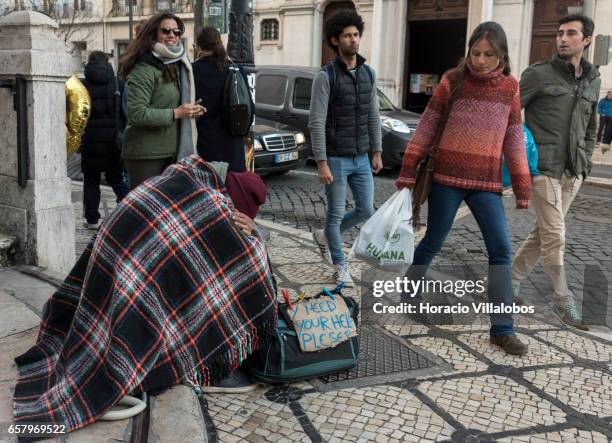 Beggar covers himself with a blanket while asking for help by via a cardboard sign during a cold afternoon on the steps of Loreto Church at Praca...