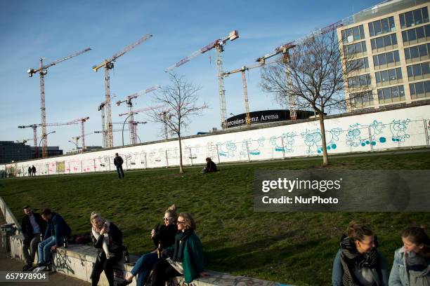 Cranes and the Mercedes-Benz Arena are seen from the park of the East Side Gallery as people enjoy the first spring sun in the district of...