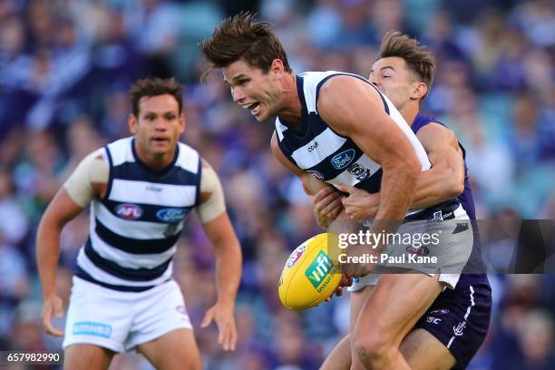 Tom Hawkins of the Cats looks to handball while being tackled by Lachie Weller of the Dockers during the round one AFL match between the Fremantle...