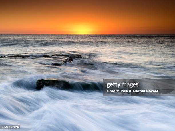 exit of the sun of orange color, on the surface of the sea, in a zone of coast with rocks and waves in movement - paisaje espectacular - fotografias e filmes do acervo