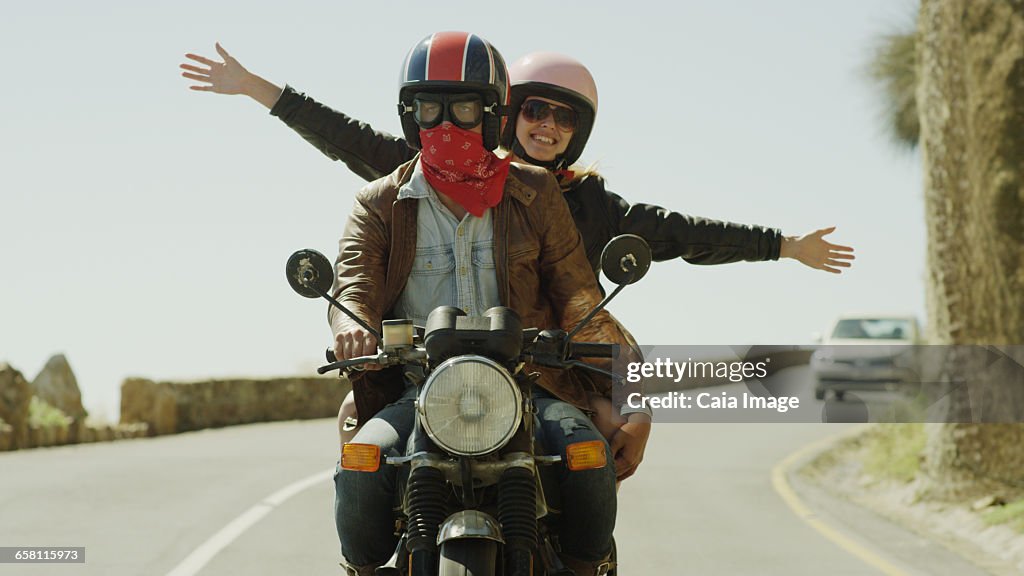 Exuberant young woman riding motorcycle on sunny road