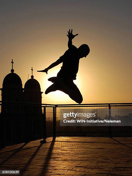 silhouette of a man jumping on the roof of a building at sunset - salto agulha imagens e fotografias de stock