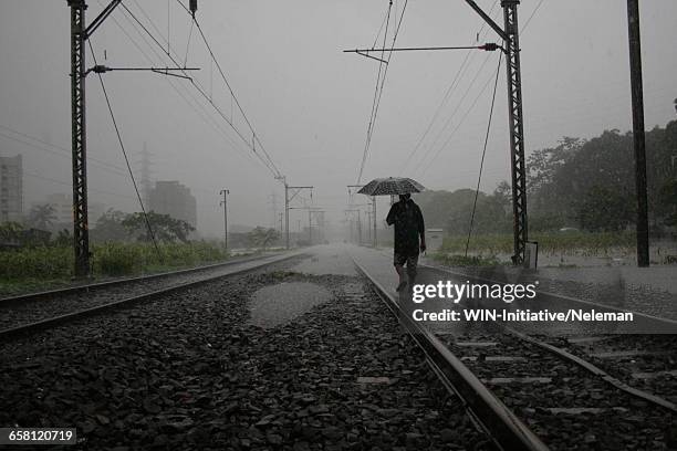 a man walking along a flooded single railway track, india - mumbai rain stock pictures, royalty-free photos & images