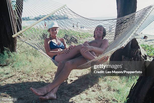 English tennis player John Lloyd and his partner and future wife, American tennis player Chris Evert pictured lying together in a hammock beside a...