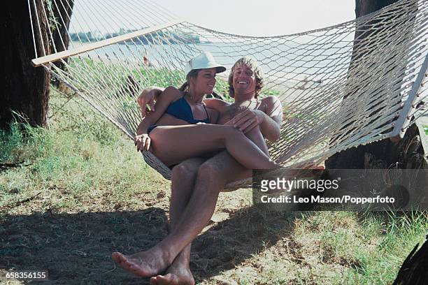 English tennis player John Lloyd and his partner and future wife, American tennis player Chris Evert pictured lying together in a hammock beside a...