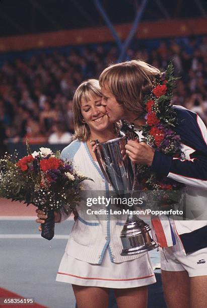 English tennis player John Lloyd kisses his wife, American tennis player Chris Evert as he holds the trophy after the pair won the Love Doubles...