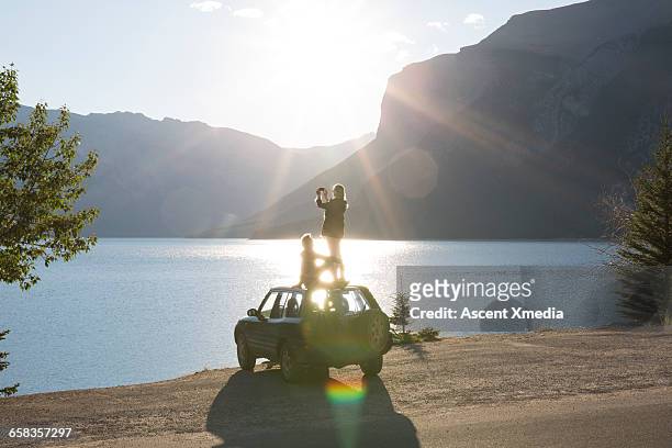 woman takes pic from car roof while man relaxes - escapismo foto e immagini stock