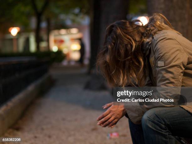 young woman sitting on a bench looking down at night - abuse fotografías e imágenes de stock