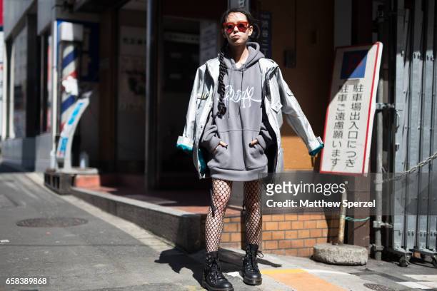 Guest is seen on the street wearing a silver rain jacket, grey hoodie, fishnet tights, and black boots during Tokyo Fashion Week on March 22, 2017 in...