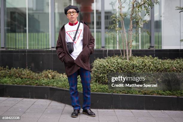 Guest is seen on the street wearing a black beret, white Guess shirt, brown coat, and blue pants during Tokyo Fashion Week on March 23, 2017 in...