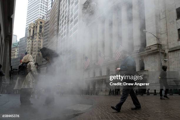 People walk past the New York Stock Exchange as steam is expelled from a manhole, March 27, 2017 in New York City. Today marked the eighth session in...