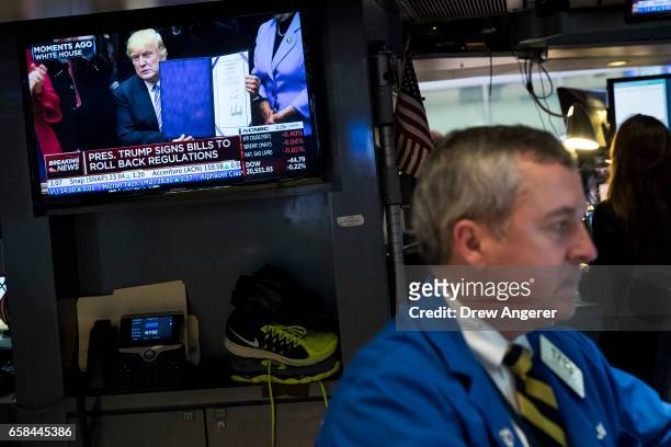 Trader works at his desk while a television monitor shows President Donald Trump after he signed four bills that reverse Obama-era regulations and...