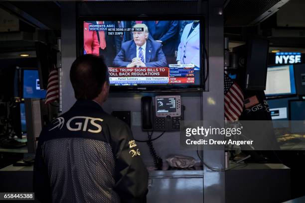 Trader watches a television monitor showing President Donald Trump after he signed four bills that reverse Obama-era regulations and rules on...