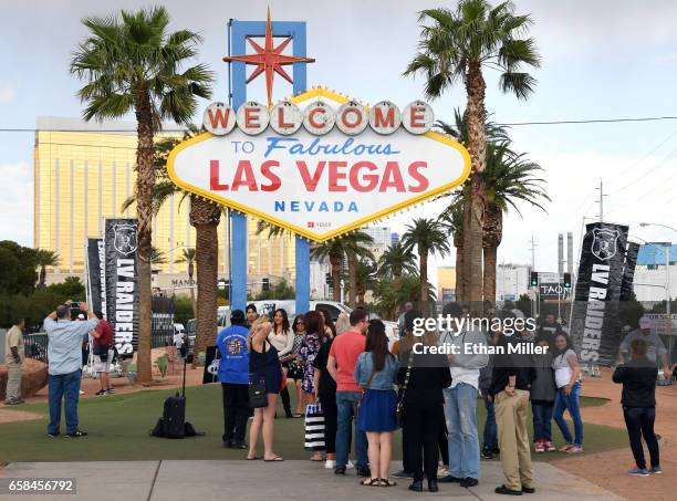 Visitors line up to take photos in front of the Welcome to Fabulous Las Vegas sign after Oakland Raiders fans placed team banners in the background...