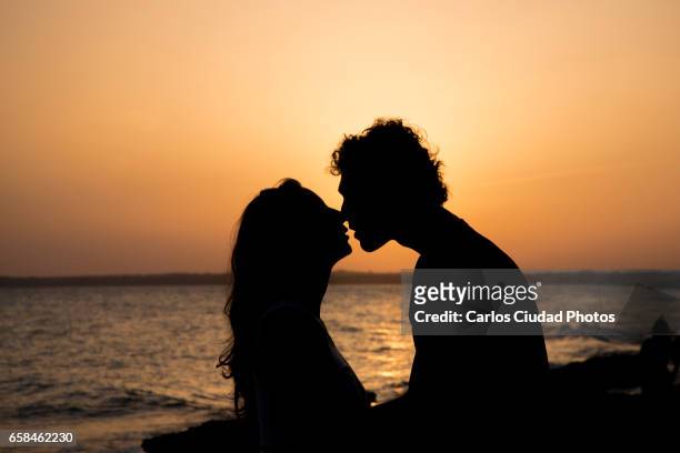 silhouette of couple kissing at sunset on the beach - couples romance imagens e fotografias de stock