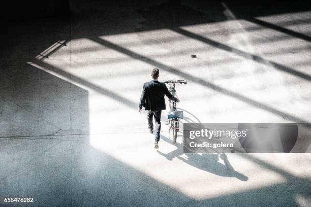 bearded elegant businessman going with bycicle on square - abstract architecture and people stock pictures, royalty-free photos & images