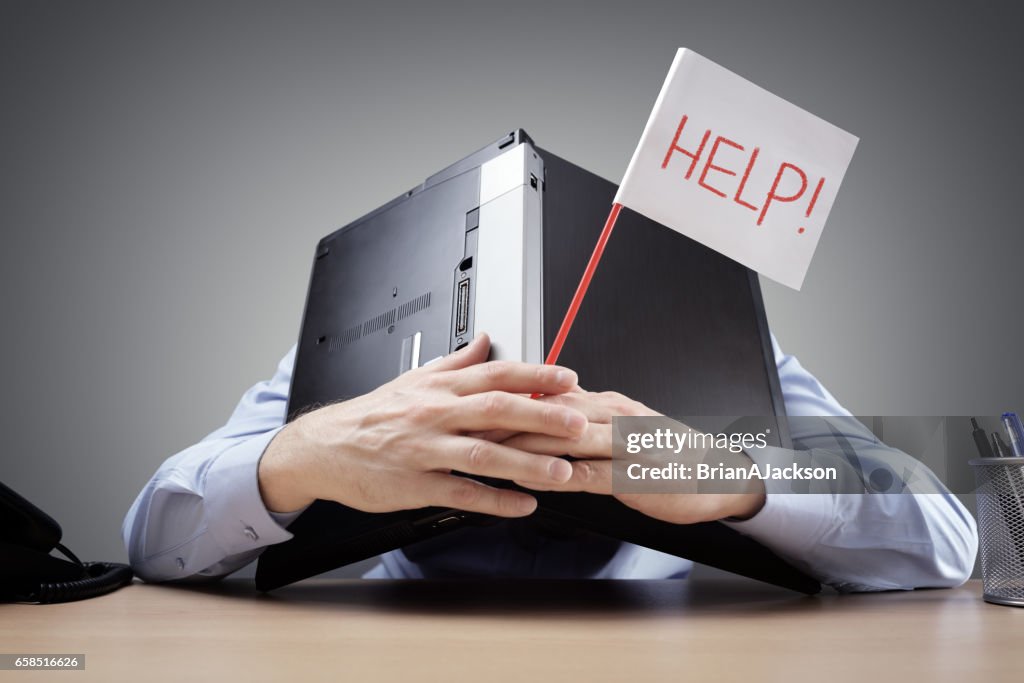 Businessman burying his head uner a laptop asking for help