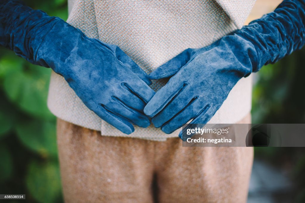 Close-up of hands in gloves of young woman in green garden on the evening