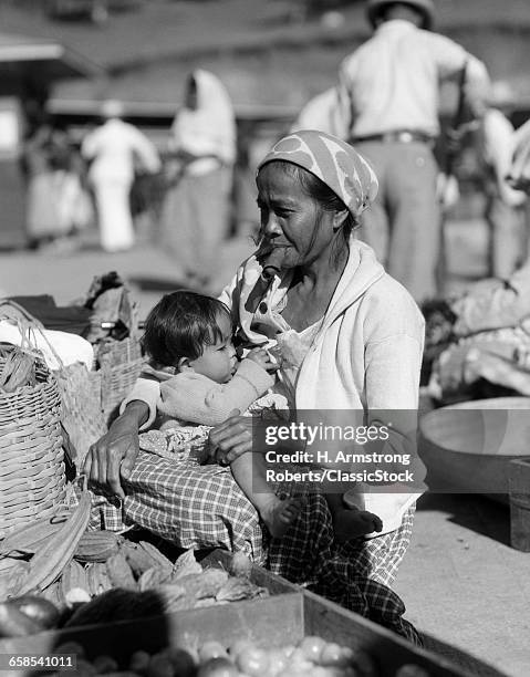 1920s 1930s WOMAN MOTHER SITTING SMOKING CIGAR CHEROOT HOLDING BABY CHILD IN MARKET PLACE BAGUIO PHILIPPINES